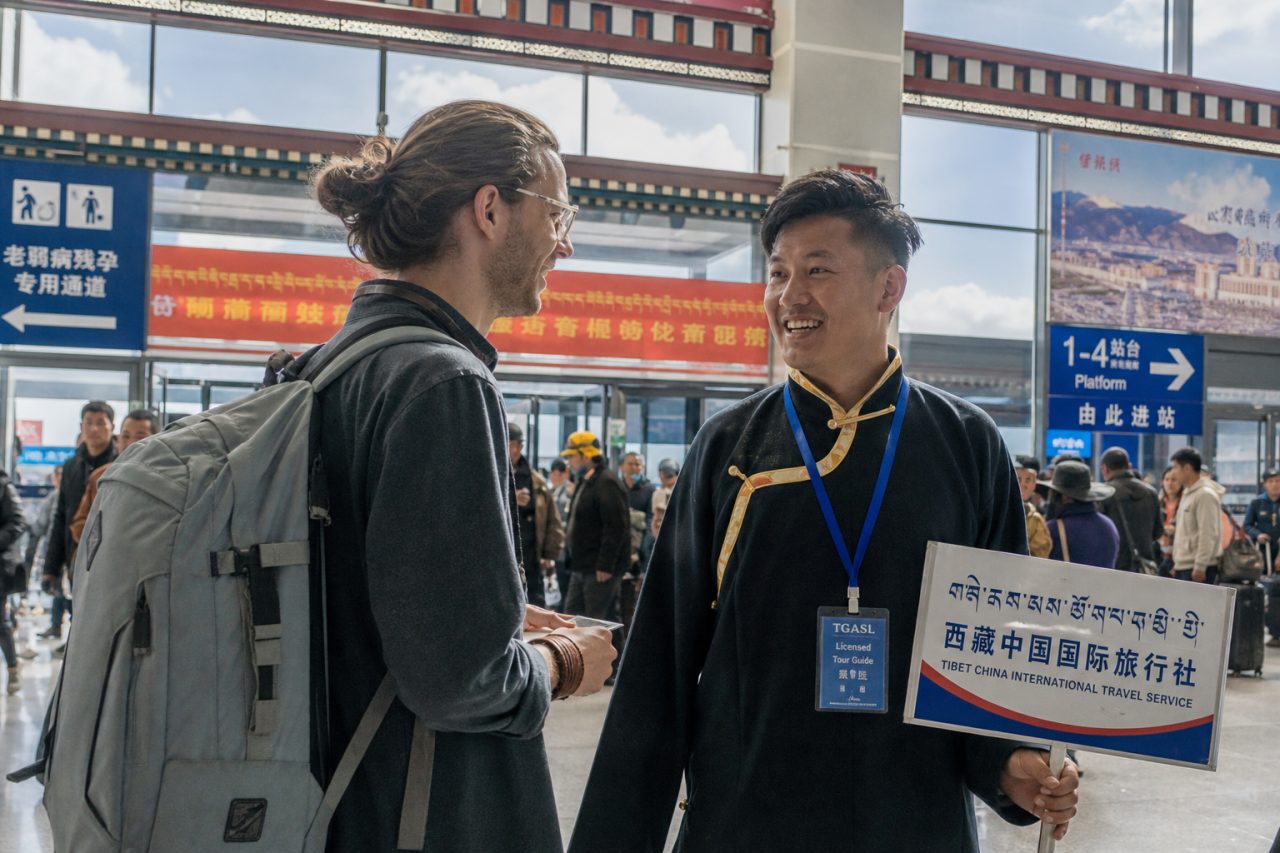 An international traveler meets a local guide in Lhasa while travel documents are checked before entering Tibet.