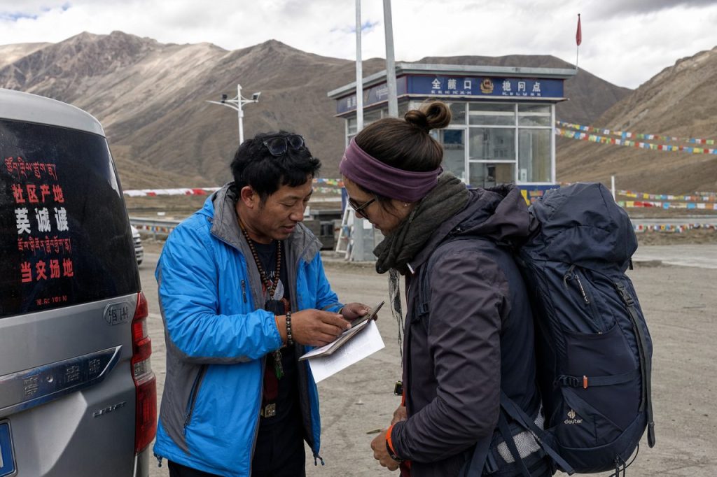 Guide checking traveler documents beside a tour vehicle during a practical Tibet travel transfer